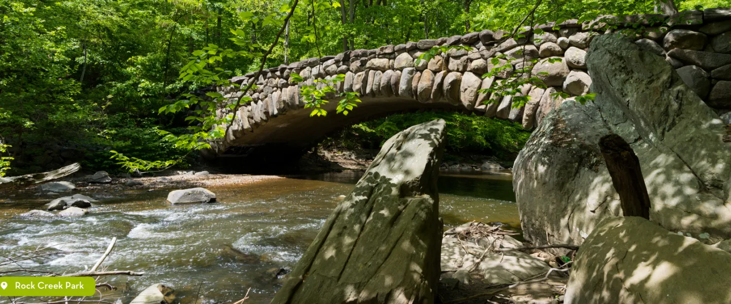 Water running down a stream at Rock Creek Park under a large stone bridge.